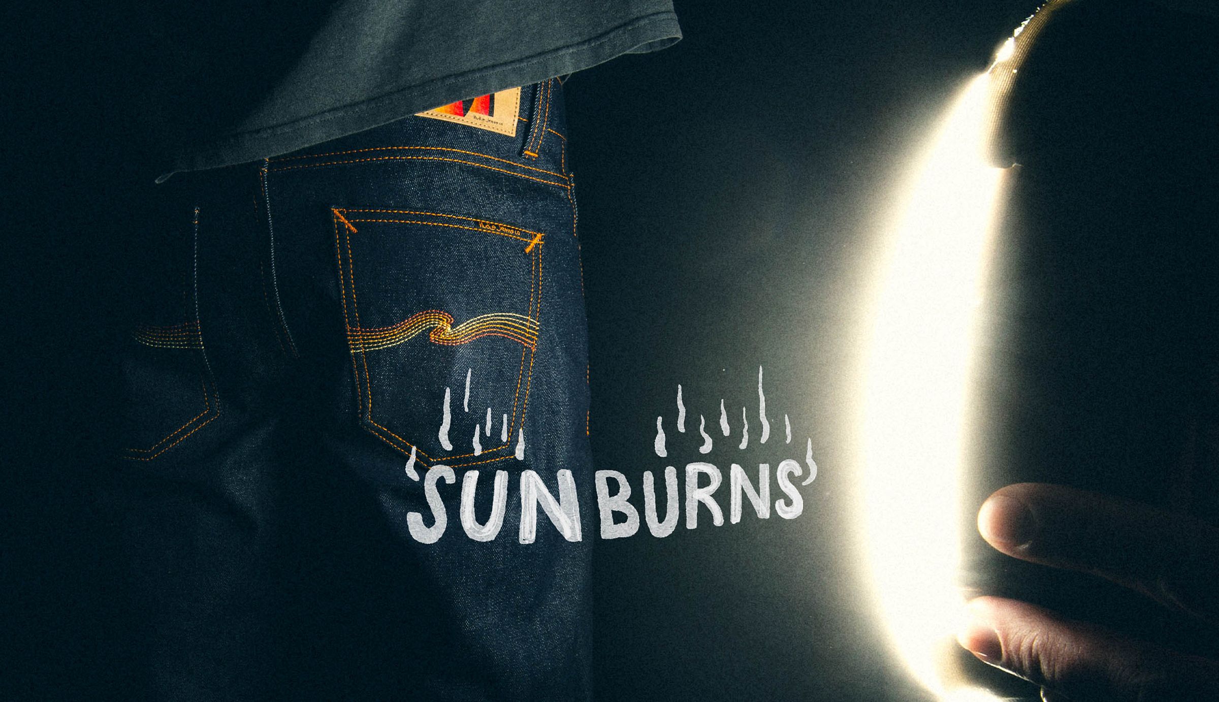 Close-up of a person in jeans with "SUNBURNS" text and a bright light source on the right, creating a dramatic contrast.