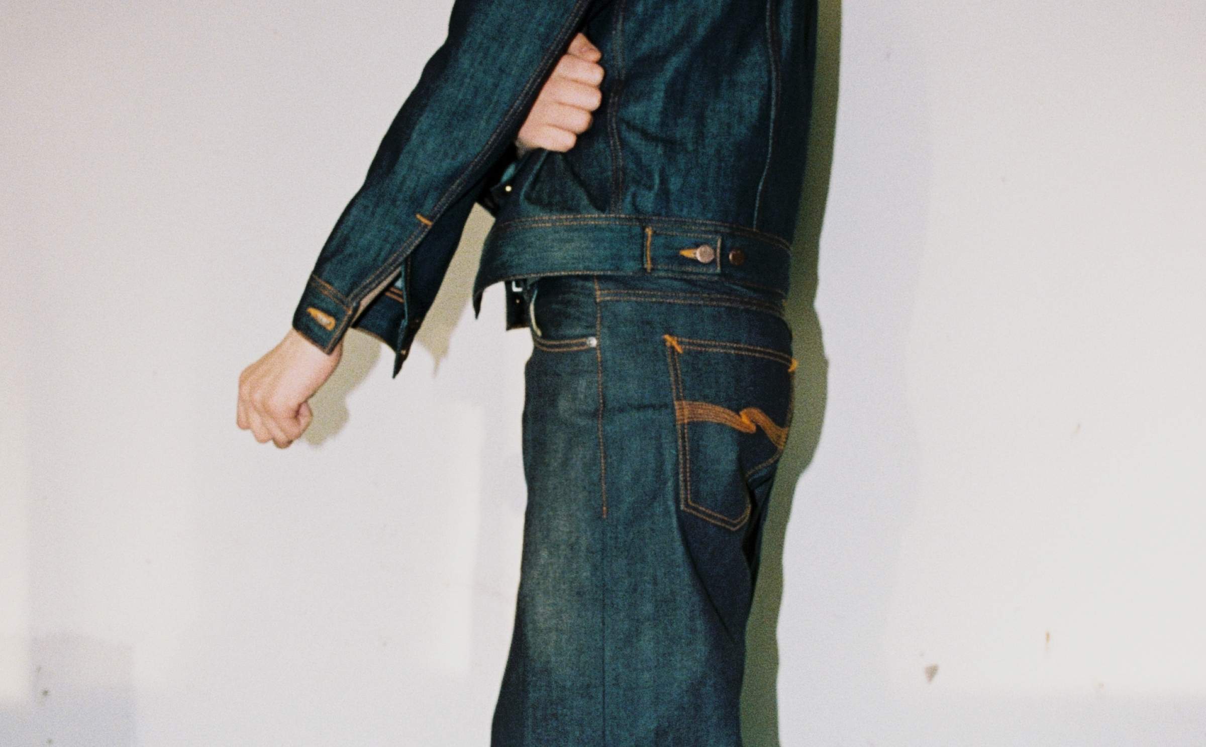 Side view of model wearing Nudie Jeans Kaihara dry selvedge denim jacket and matching jeans with contrast stitching.
