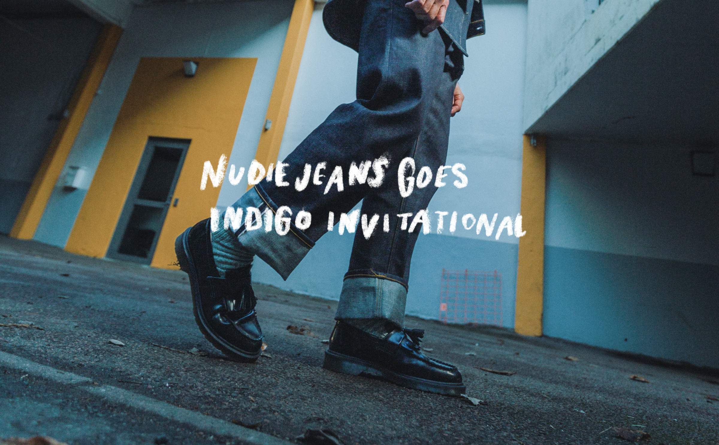 Person in denim walking, wearing black shoes, with "Nudie Jeans Goes Indigo Invitational" text overlay. Urban background with yellow accents.