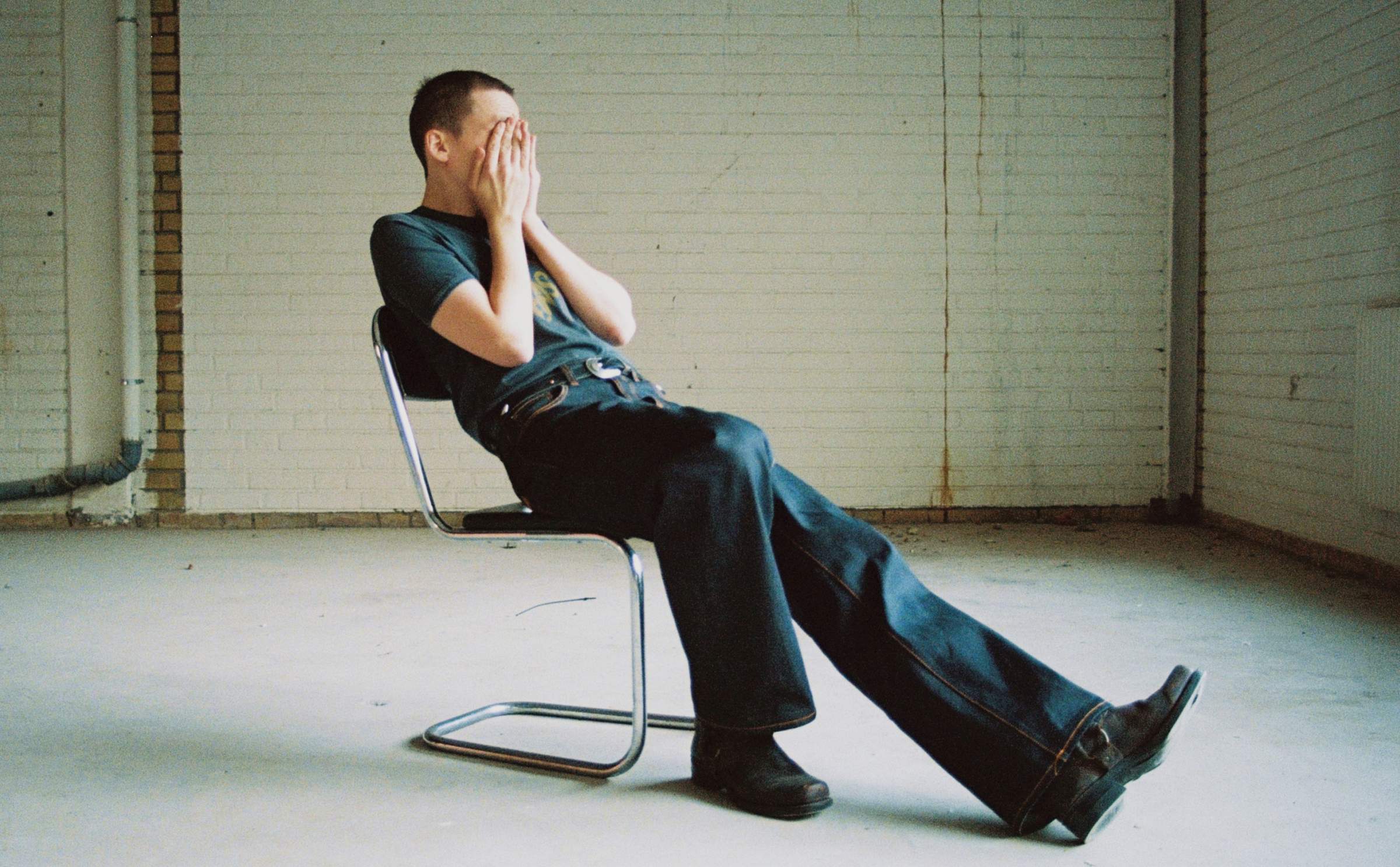 Model in Nudie Jeans dry raw selvedge denim jeans and tee leans back on a chair, hands covering face.