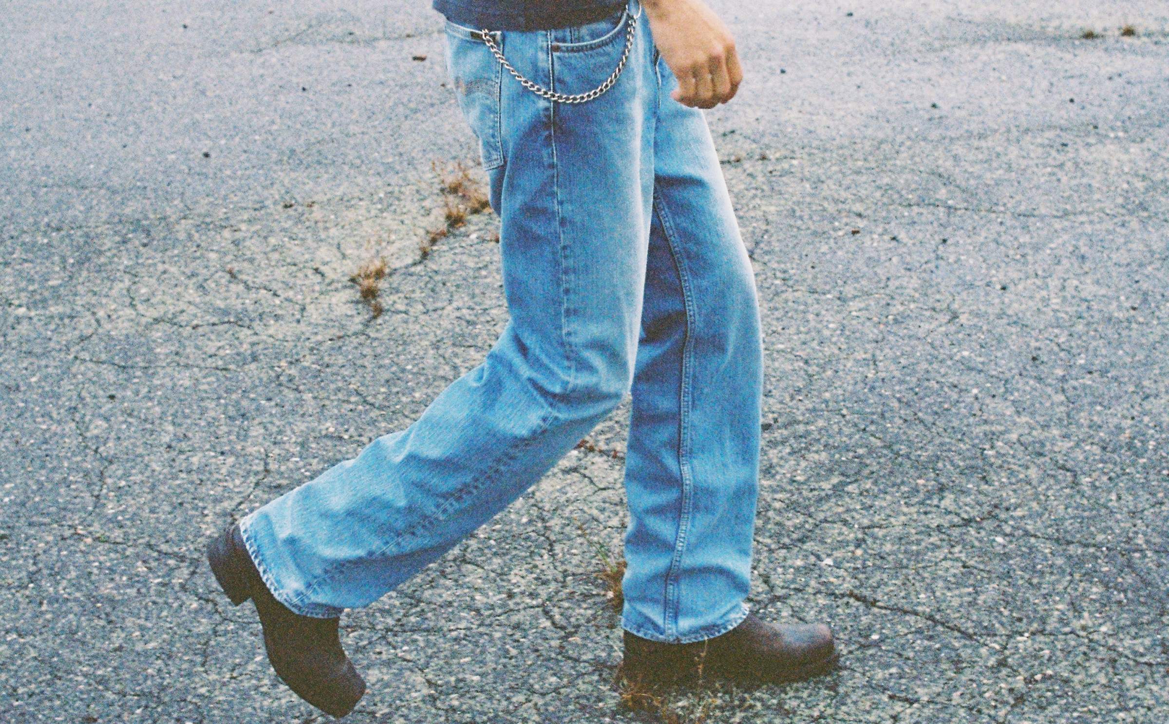 Model walking in light blue Nudie Jeans prewashed denim with silver wallet chain and brown leather boots.