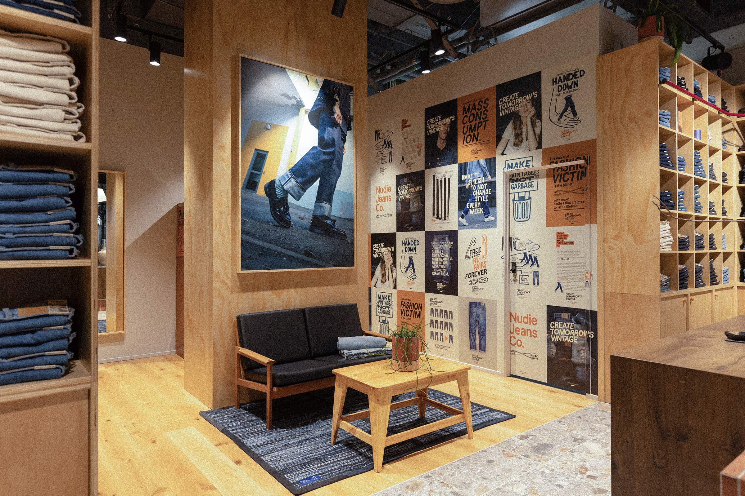 Clothing store interior with wooden shelves, a seating area, and walls adorned with colorful posters and folded jeans.