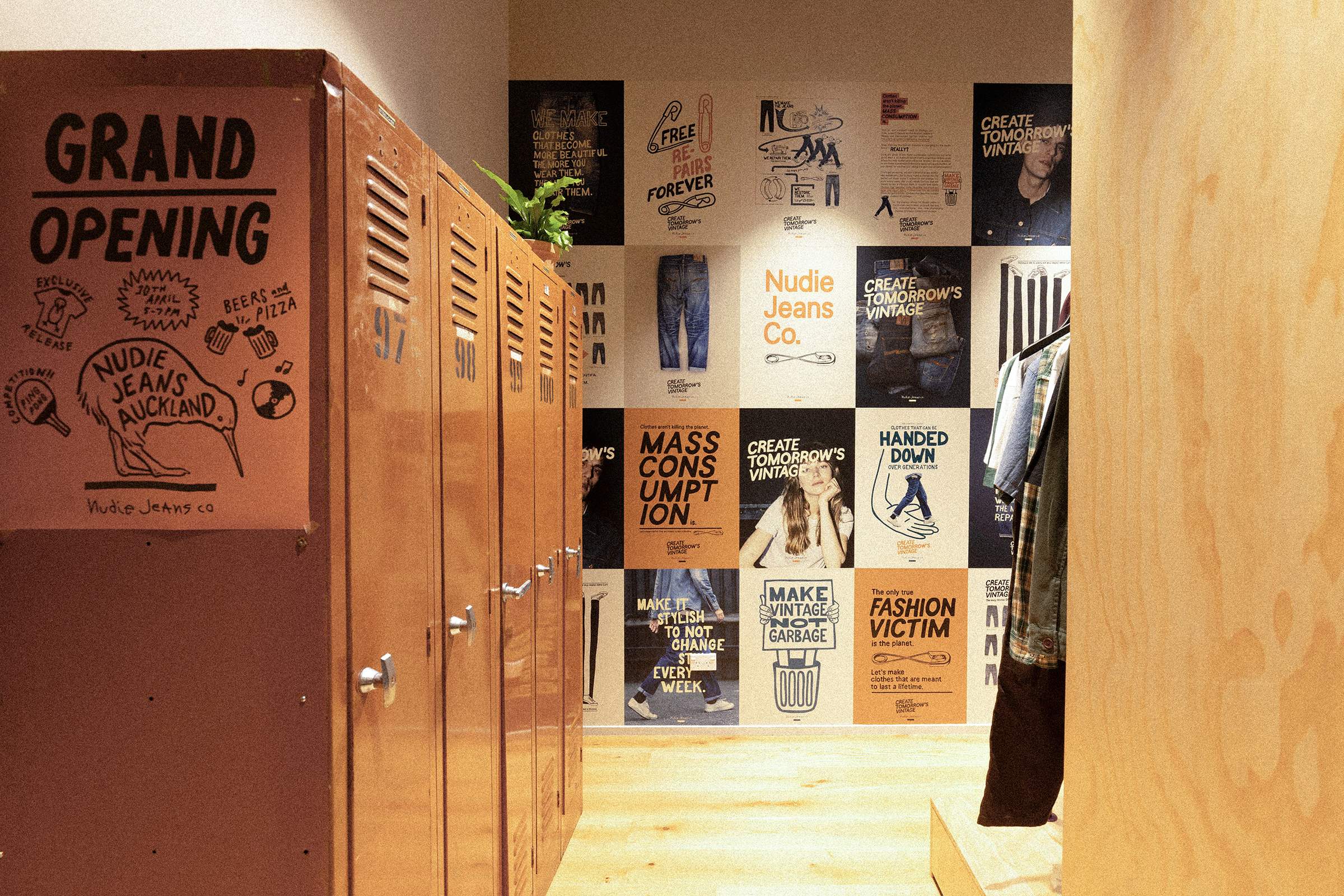 Hallway with red lockers and a wall of colorful posters. Text on lockers reads "Grand Opening." Clothing hangs on the right.