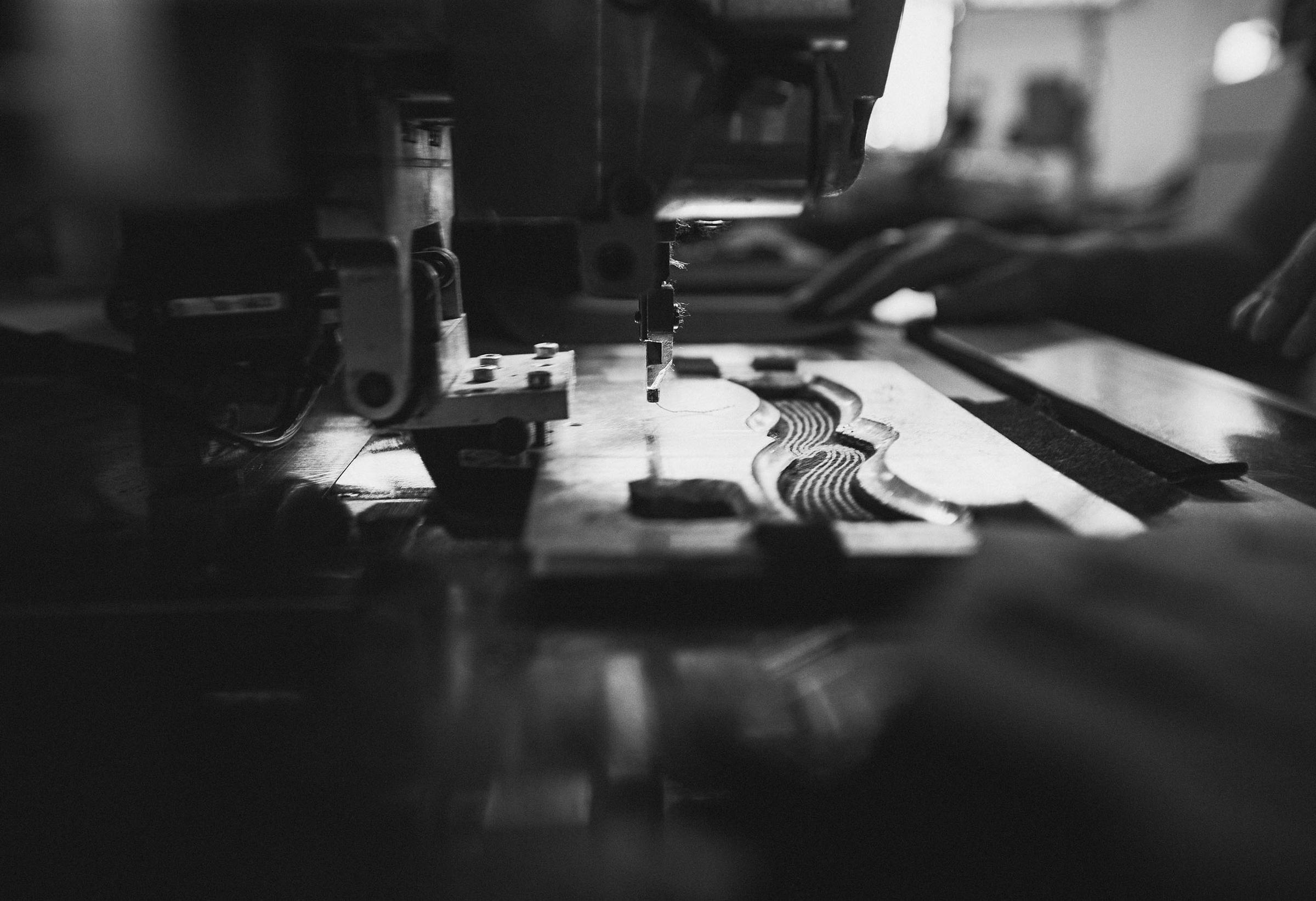 Black and white image of a close-up view of a machine in operation, with hands adjusting components, highlighting industrial precision.