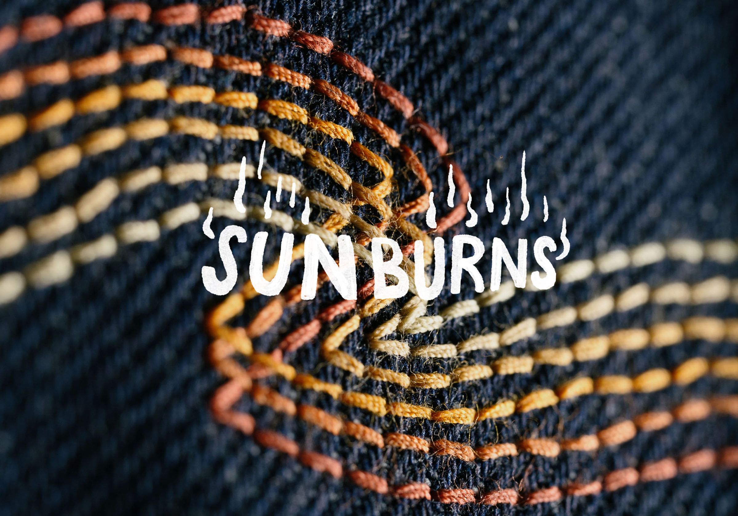 Close-up of colorful embroidered waves on dark fabric with the text "SUN BURNS" in white, stylized with flame-like accents.
