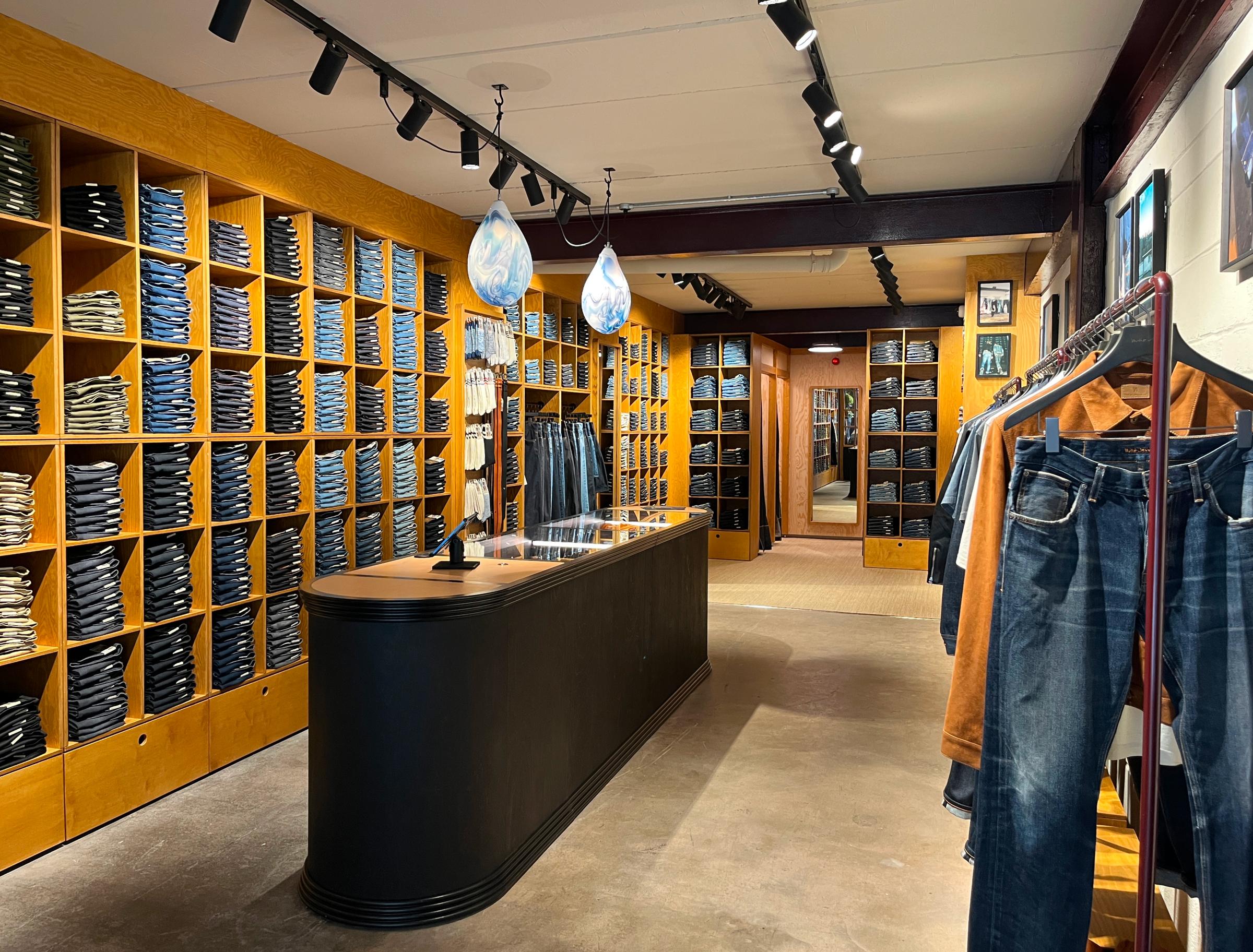 Clothing store interior with shelves of folded jeans, a central black counter, hanging lights, and racks displaying jeans and shirts.