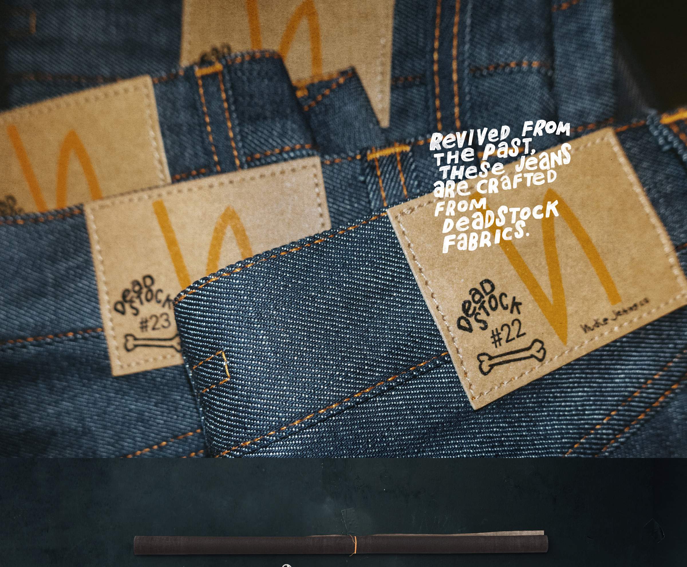Close-up of denim jeans with brown labels reading "Deadstock #23" and "#22," featuring orange stitching and text promoting deadstock fabric use.