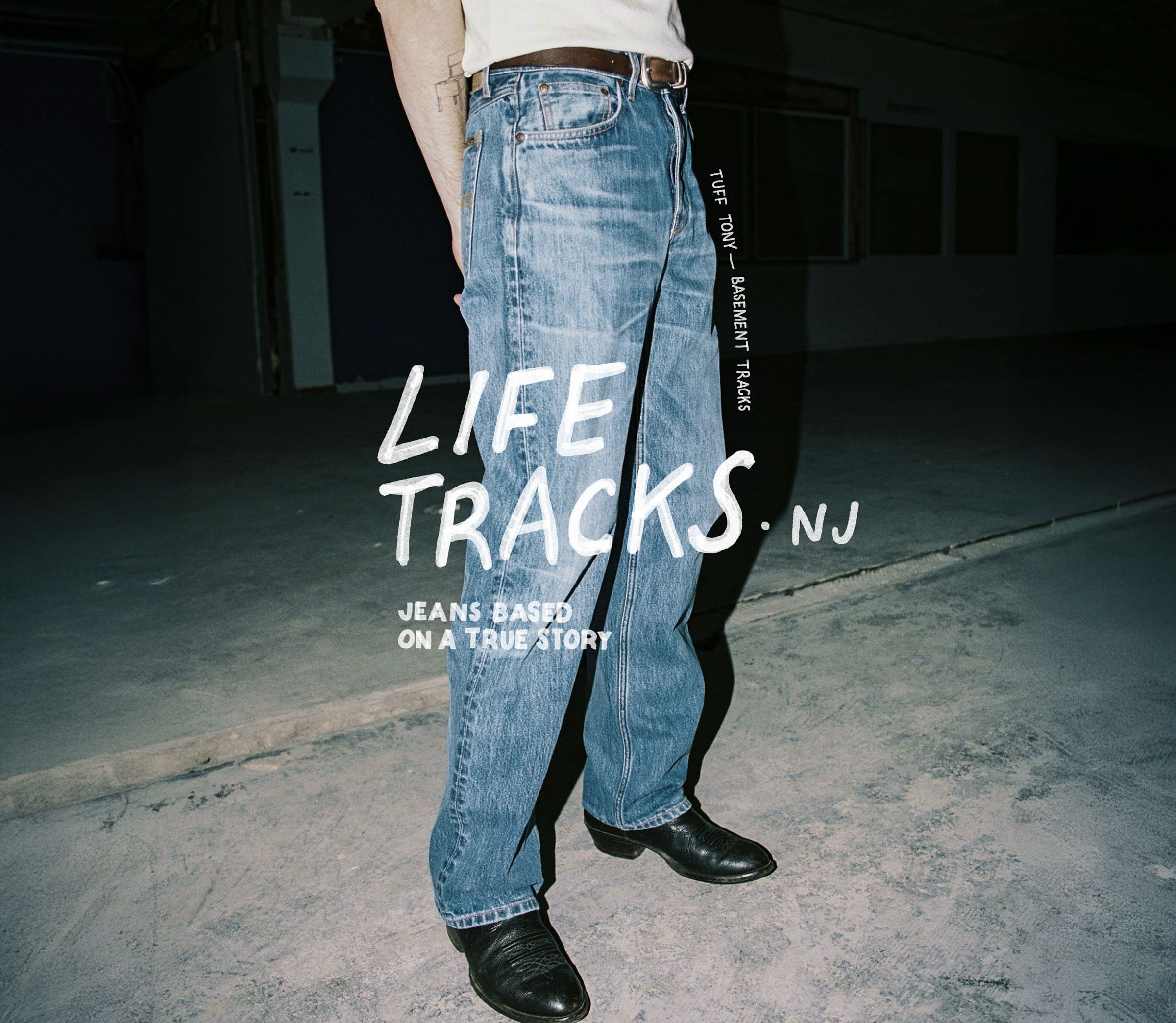 Person wearing blue jeans and black shoes stands in a dimly lit space. Text on jeans reads, "TRUE TRACKS BARRETT TRACKS." Text overlay: "LIFE TRACKS NJ."