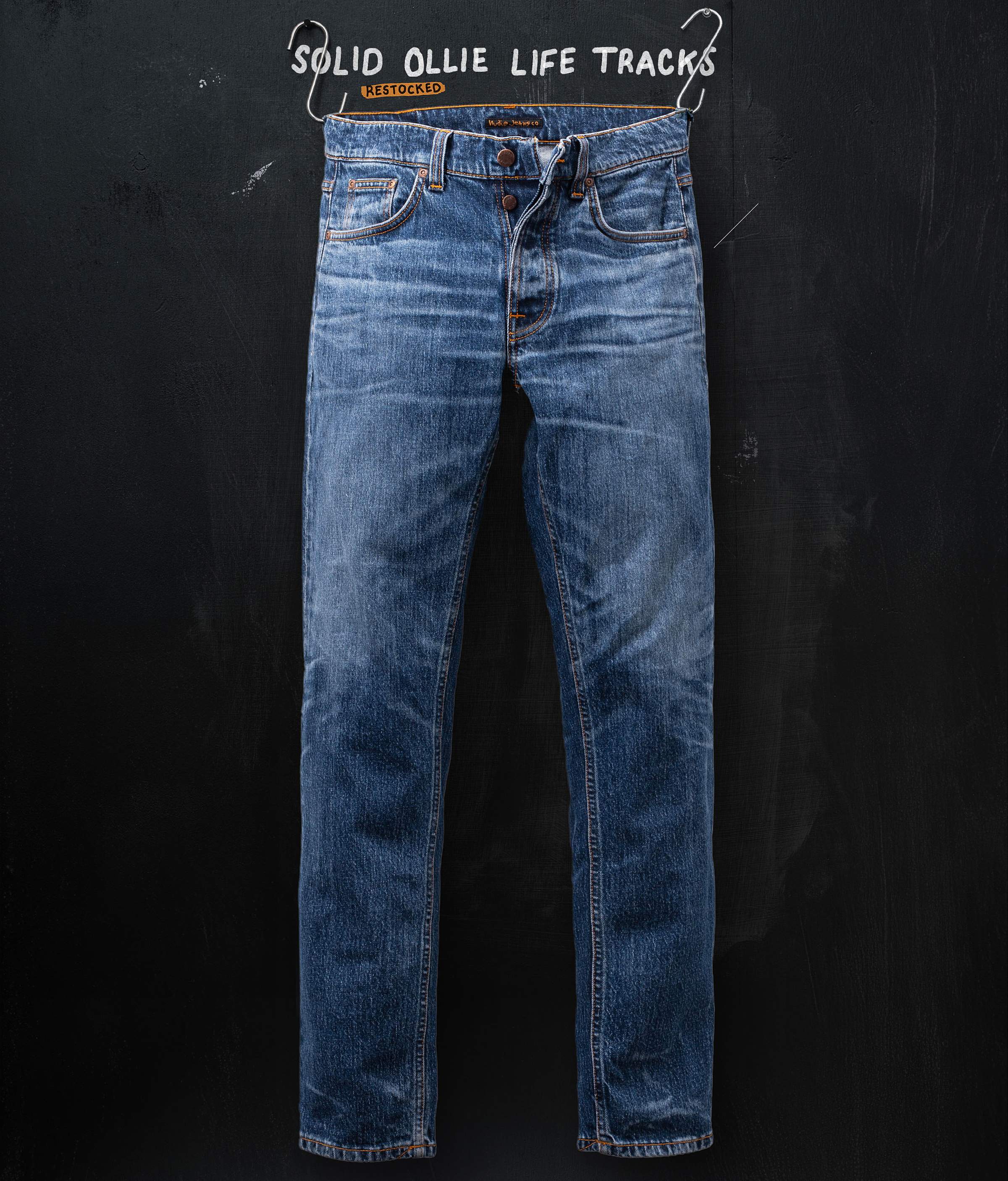 Blue denim jeans hanging against a dark background, with the text "Solid Ollie Life Tracks" above.