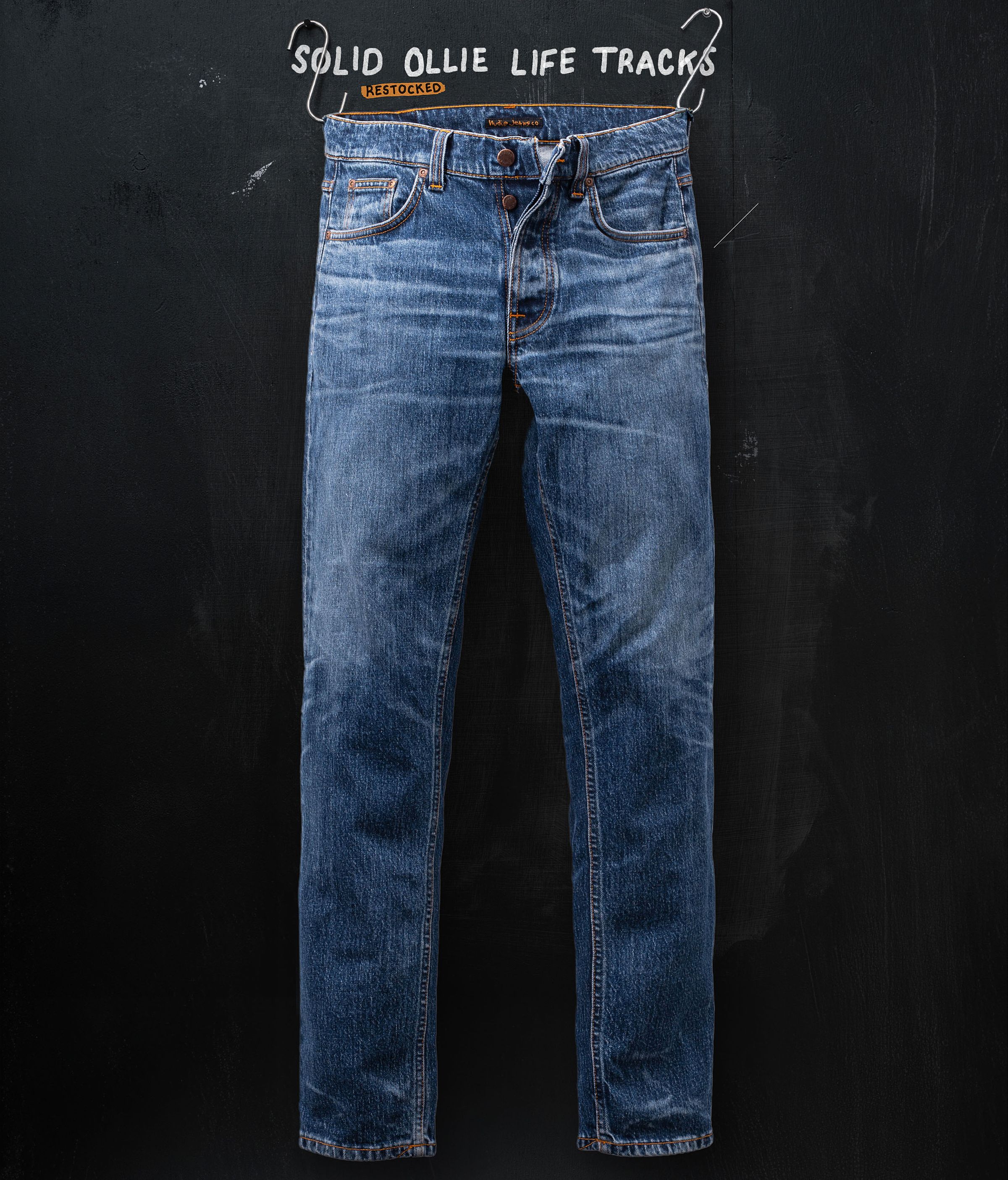 Blue denim jeans hanging against a dark background, with the text "Solid Ollie Life Tracks" above.