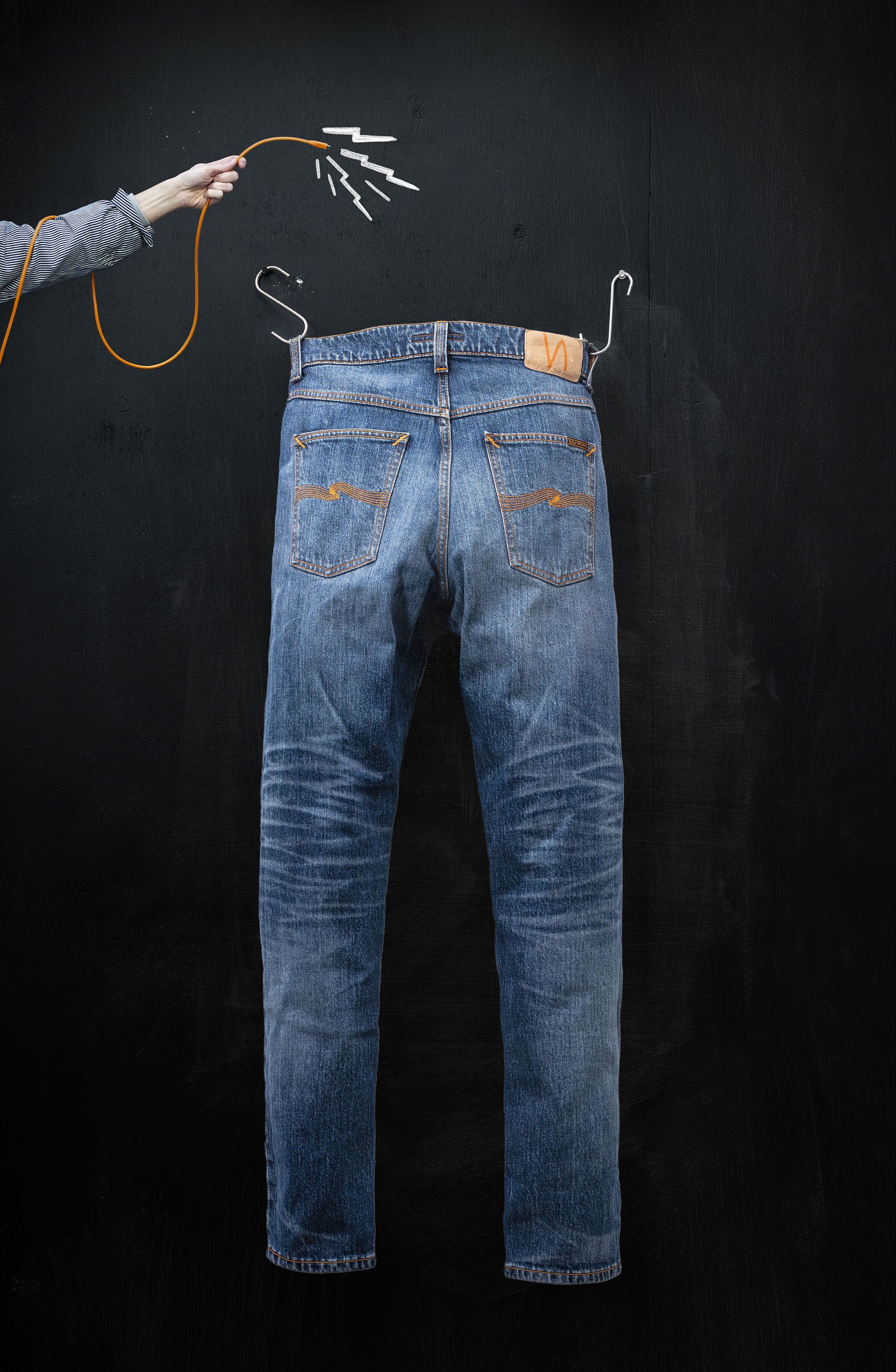 A pair of blue jeans drawn on a blackboard, with real jeans pockets and a hand holding a string above, resembling a puppet.