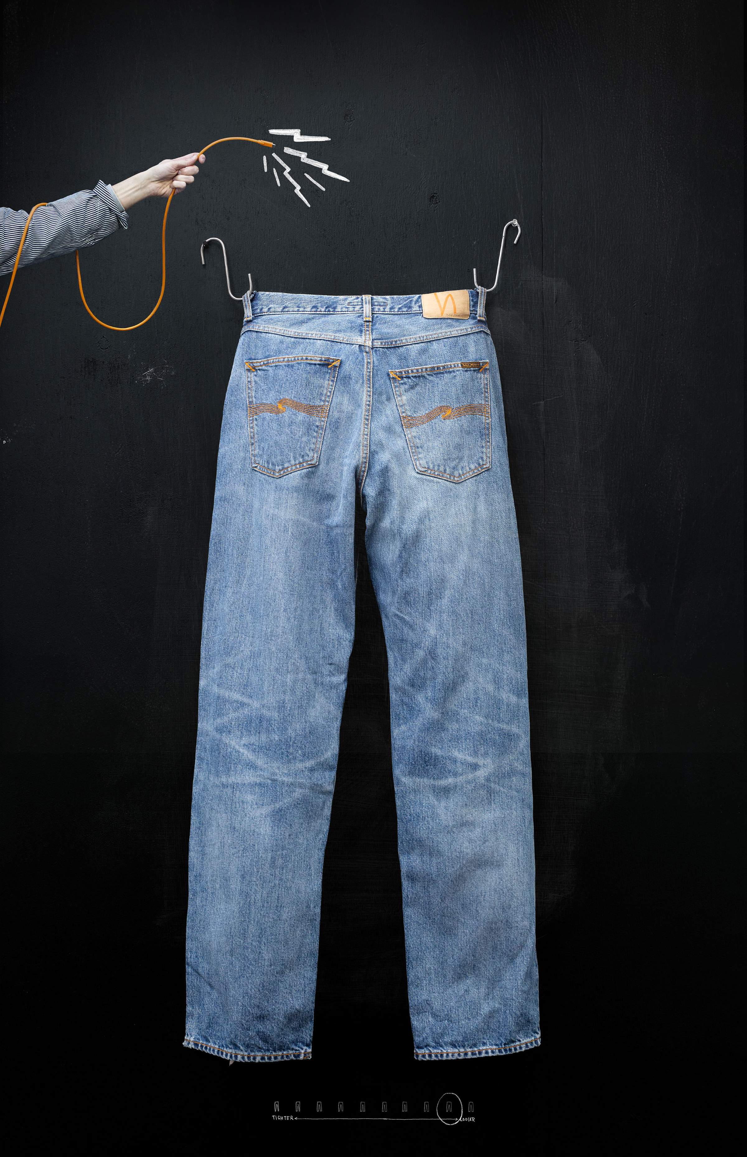 Blue jeans hanging on a black wall, with a hand holding a yellow cable connected to the jeans, creating a visual effect.