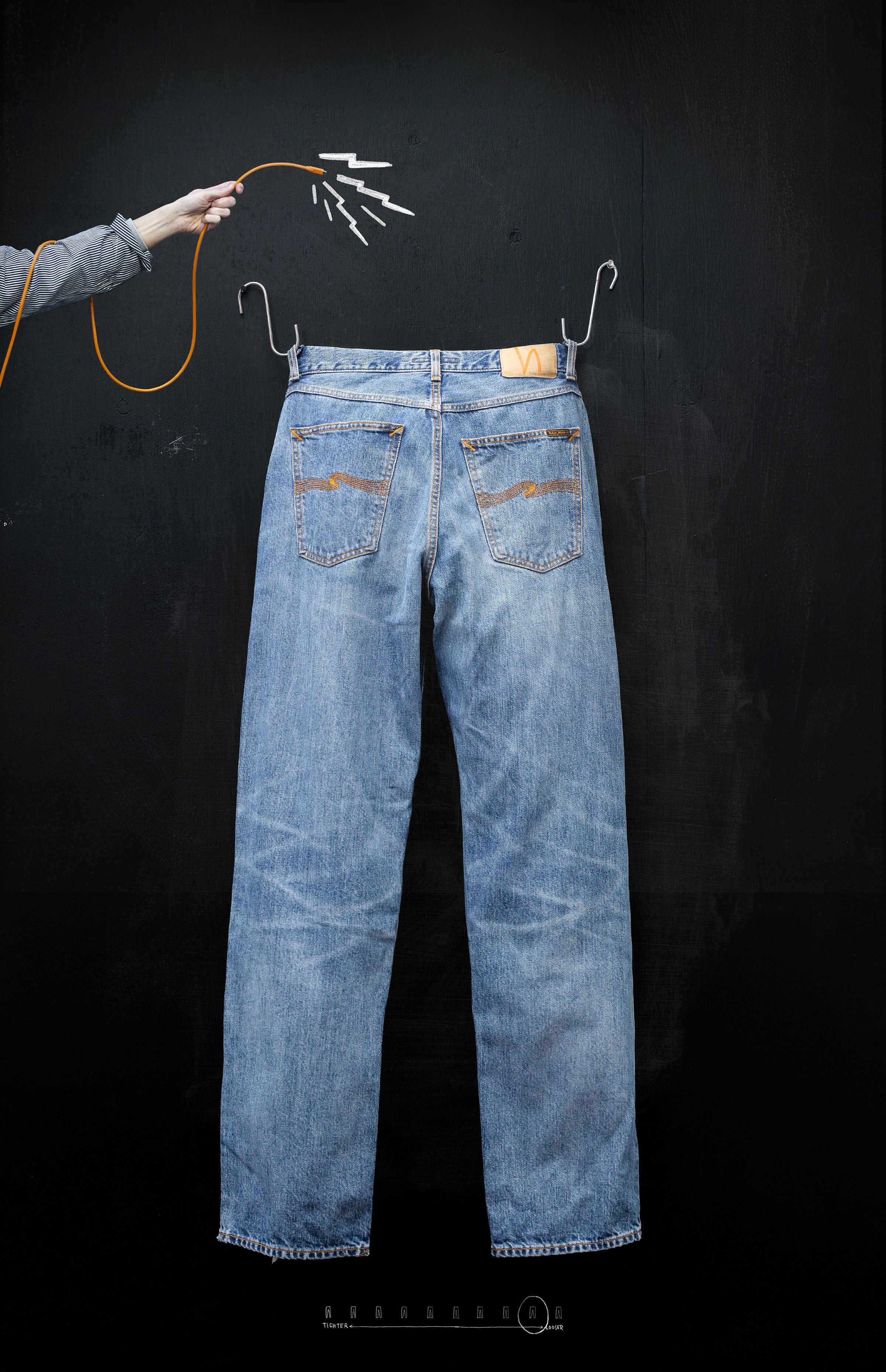 Blue jeans hanging on a black wall, with a hand holding a yellow cable connected to the jeans, creating a visual effect.