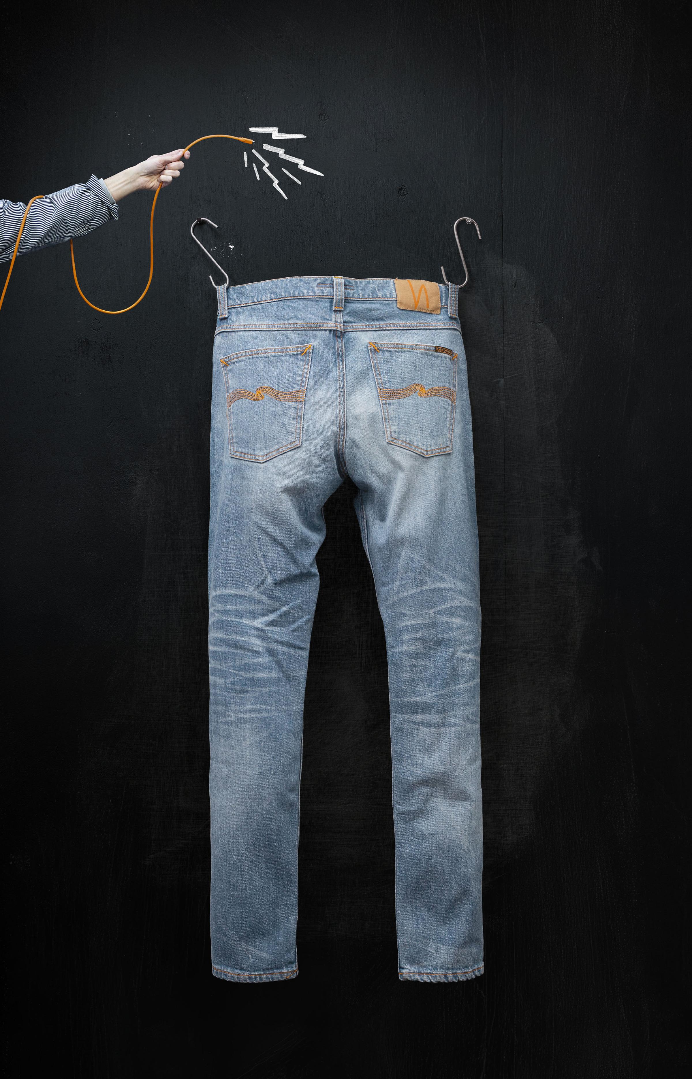 Blue jeans hanging on hooks against a dark background, with a hand holding an orange wire above them.