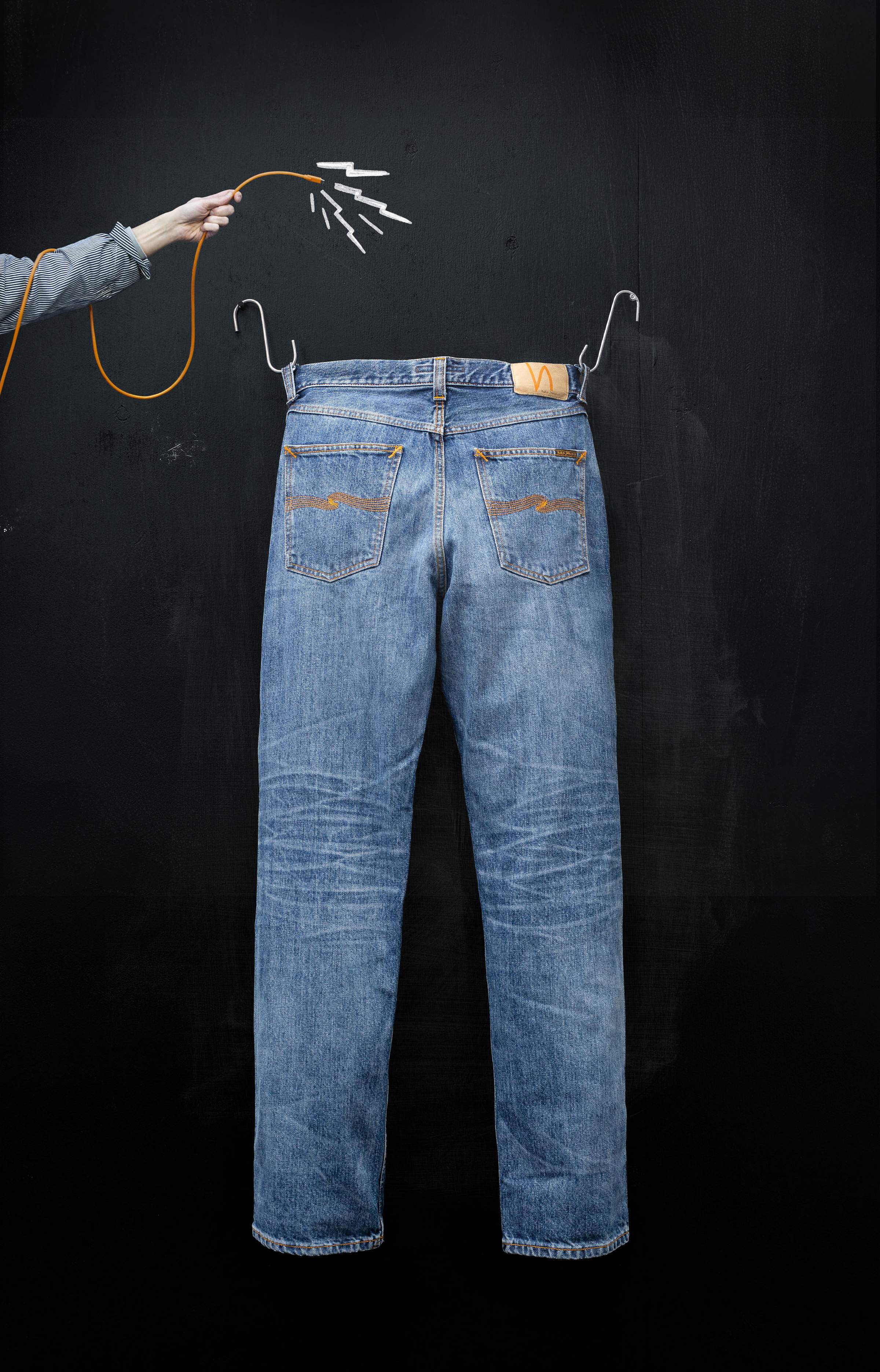 Nudie Jeans Rad Rufus raw selvedge denim hanging on a hook with a hand holding a cord and chalk lightning bolts.