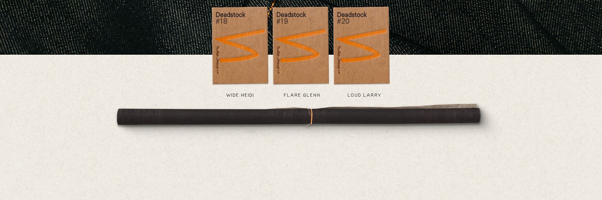 A roll of dark fabric below three cardboard labels with orange designs, labeled "Deadstock #18," "#19," and "#20," on a textured background.