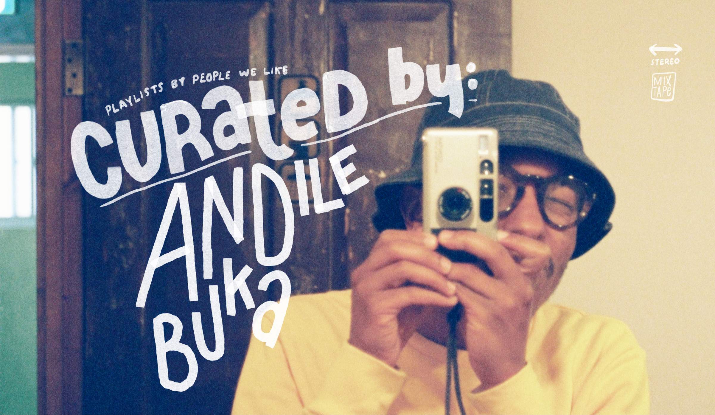Person in a yellow sweater and bucket hat takes a mirror selfie with a camera. Text reads "Curated by: Andile Buka."