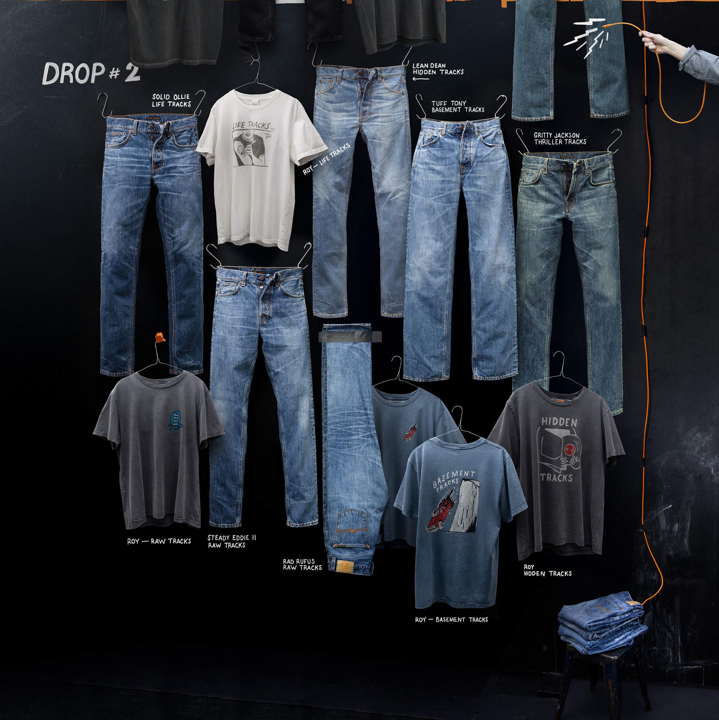 Nudie Jeans Life Tracks Drop #2 collection of denim jeans and graphic t-shirts displayed on a black chalkboard wall.