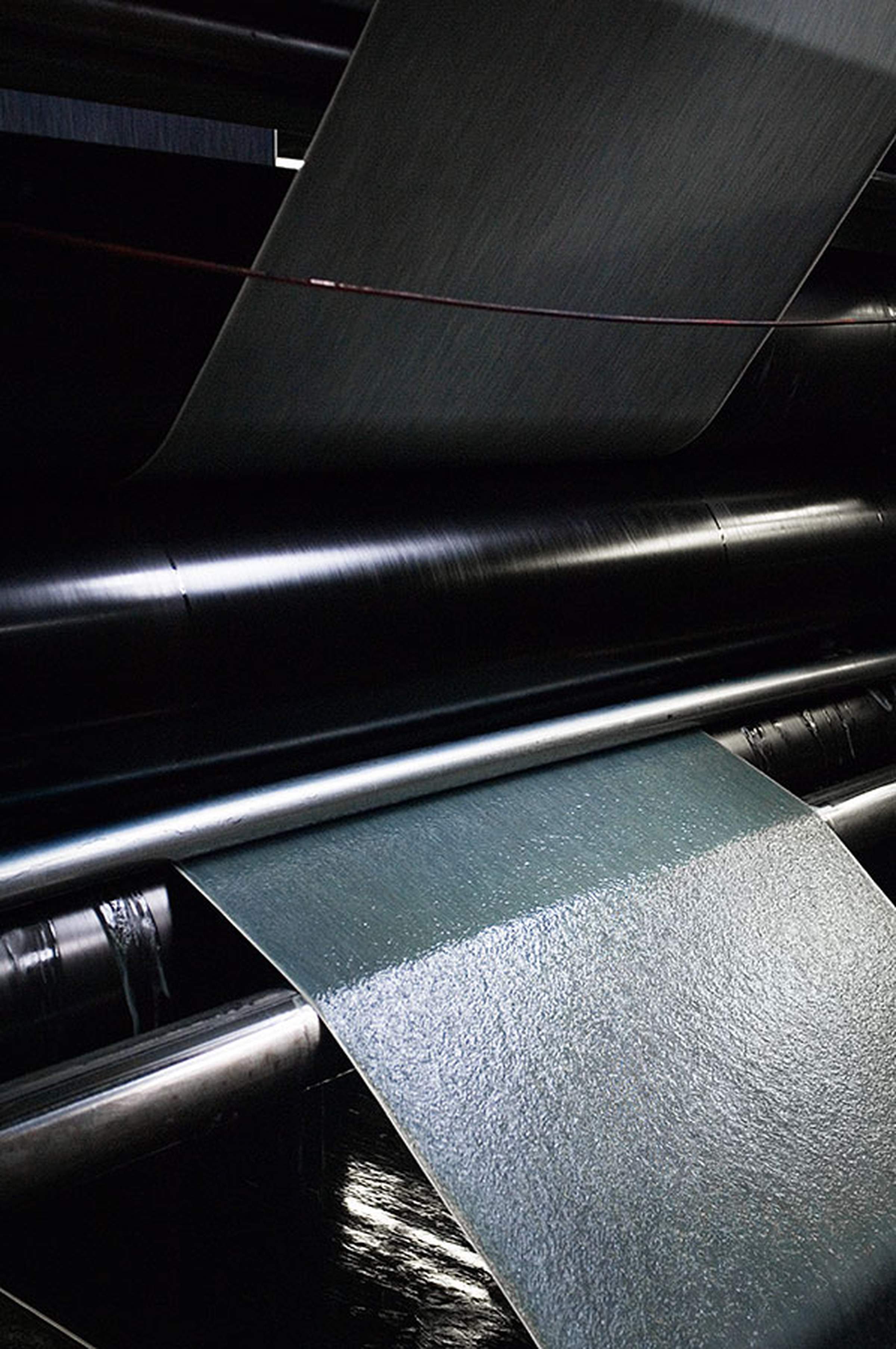 Close-up of a textile manufacturing machine with fabric sheets moving through rollers, showcasing the industrial process.