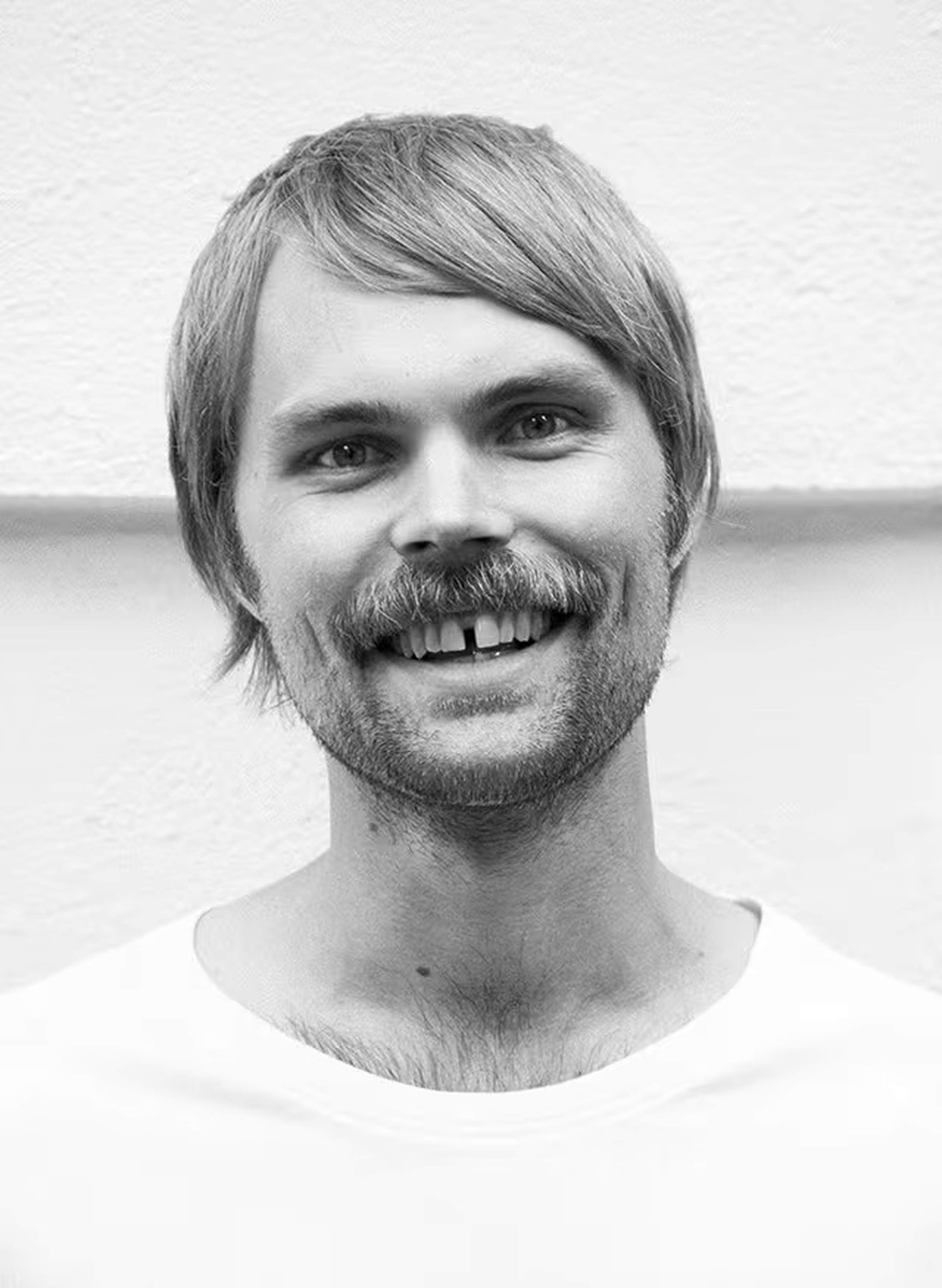Ben with a mustache and short hair, wearing a white shirt, against a plain background. Black and white photo.