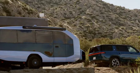 An SUV towing a Pebble Flow parked in a scenic mountainous area under a clear sky.