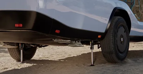 A Pebble Flow parked on sand, supported by stabilizing hydraulic jacks, with visible wheels and partial undercarriage.