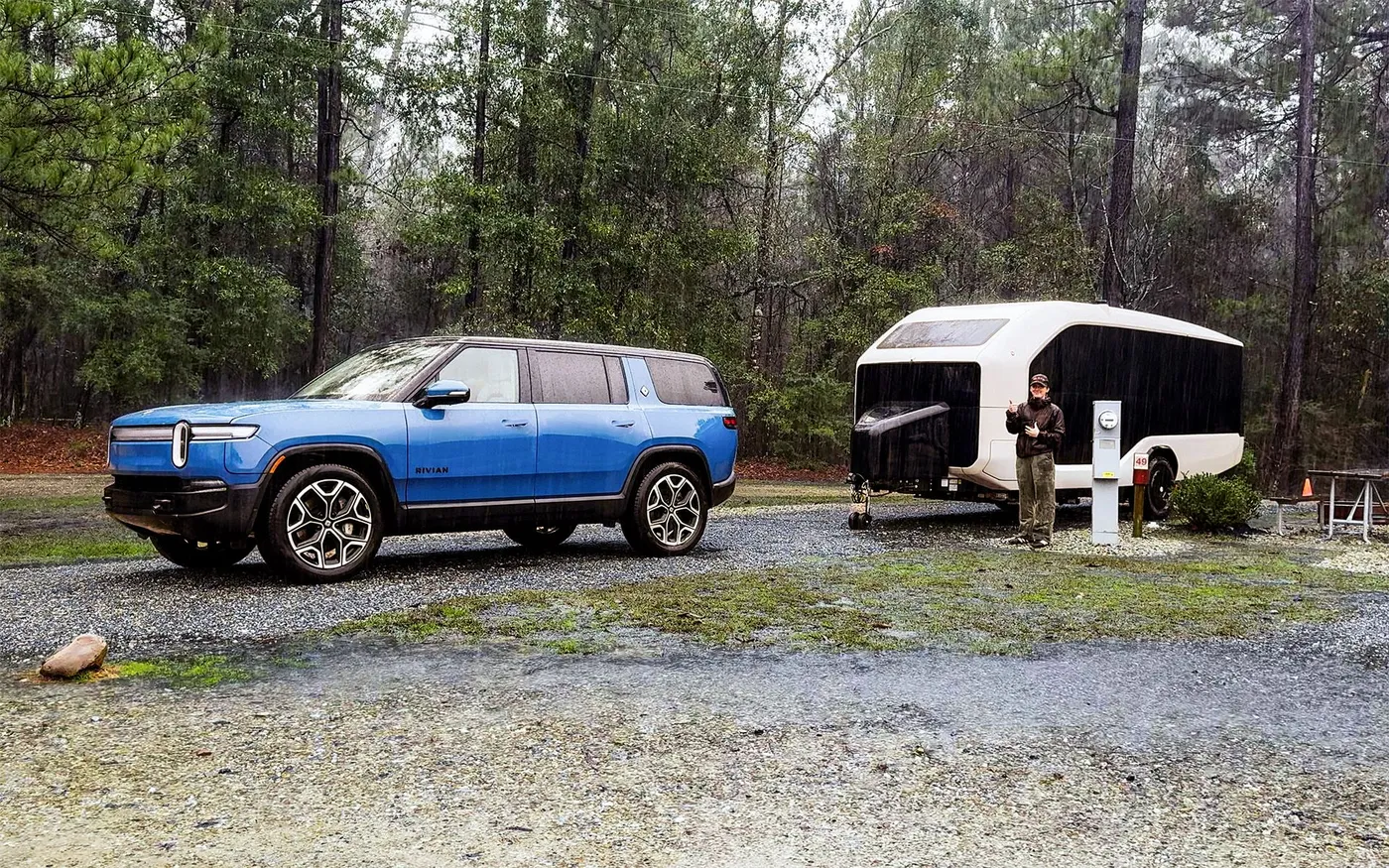 A Pebble parked behind a Rivian with a person holding an iPad in the rain