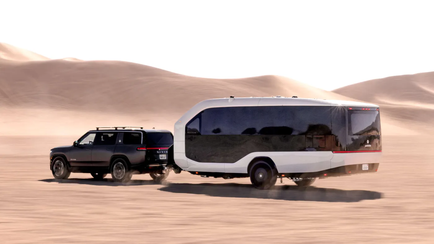 An SUV towing a Pebble Flow through a desert landscape, leaving a trail of dust behind against rolling sand dunes.