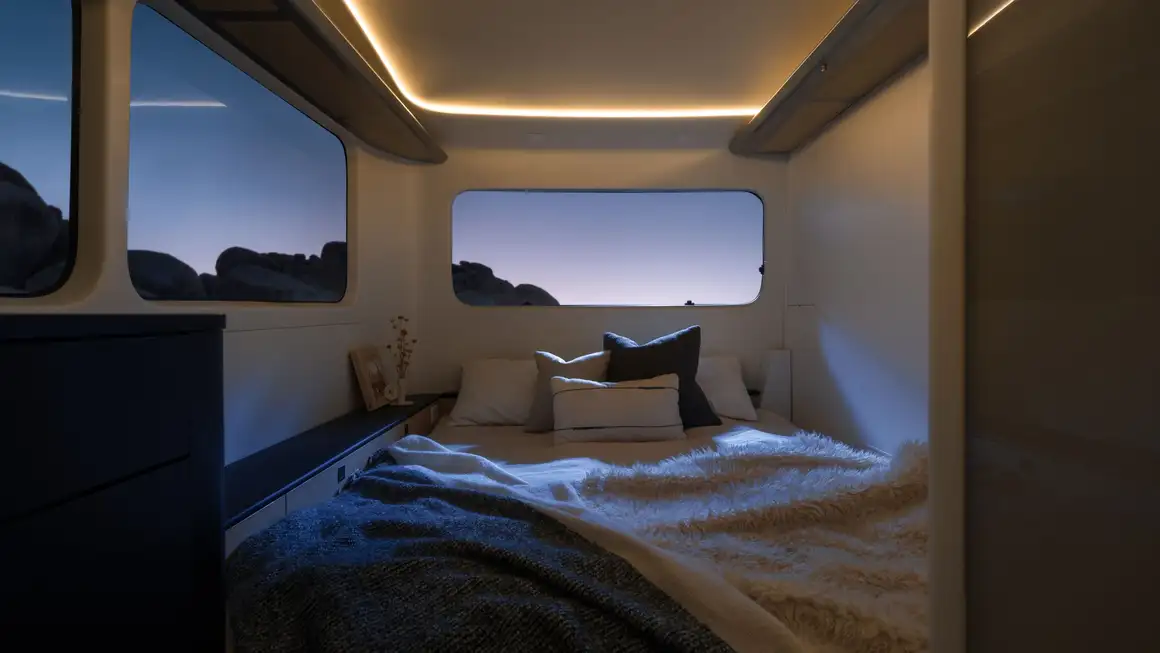 Pebble Flow interior with a neatly made bed, soft lighting, and large windows showcasing a serene evening landscape.