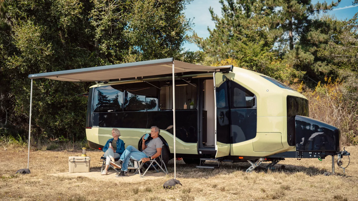 A couple sitting outside a Pebble Flow under an awning in a grassy area with trees in the background, enjoying drinks.