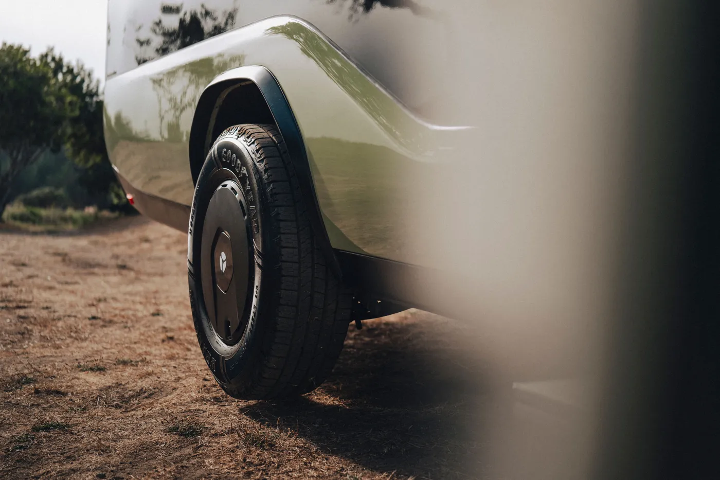 Close-up of a Pebble Flow's rear wheel with Goodyear tire, parked on dry, grassy ground.