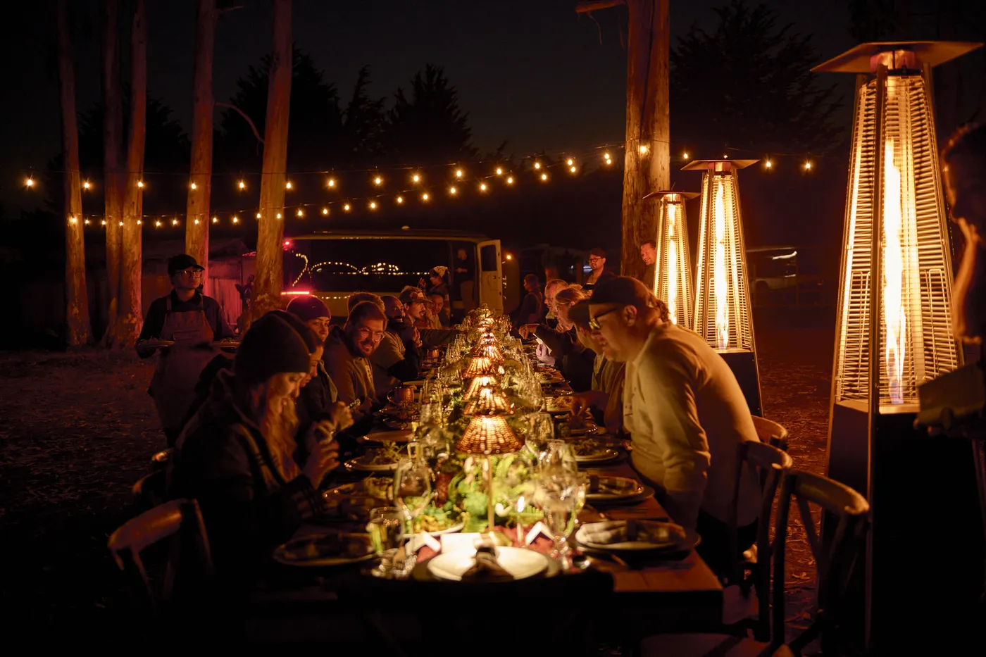 Chef Ryan cooking with a Flow in frame, or the long table under patio heaters at dusk