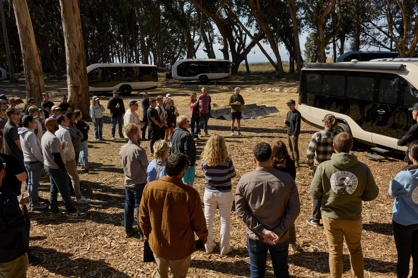 Wide candid of Bingrui or Stefan speaking in the grove with guests seated close
