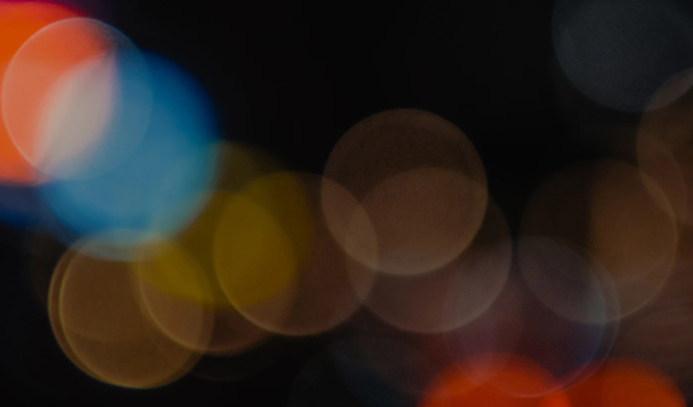 Abstract bokeh background with circular blurred lights in shades of blue, red, yellow, and brown on a dark backdrop.