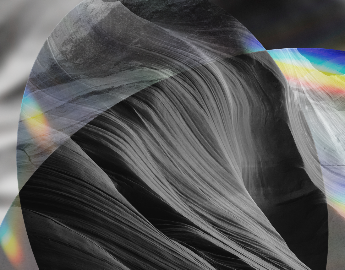 Abstract image of smooth, layered rock formations in grayscale, overlaid with translucent rainbow-colored light patterns.