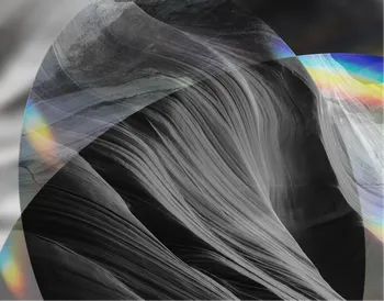 Abstract image of smooth, layered rock formations in grayscale, overlaid with translucent rainbow-colored light patterns.