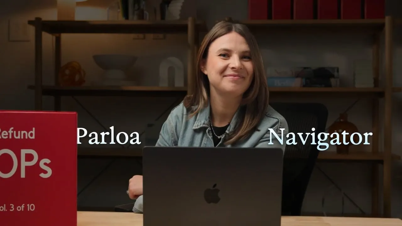 Eine lächelnde Person an einem Schreibtisch mit Laptop, umgeben von Regalen, ein rotes Schild ist teilweise sichtbar. Darüber die Wörter „Parloa“ und „Navigator“.