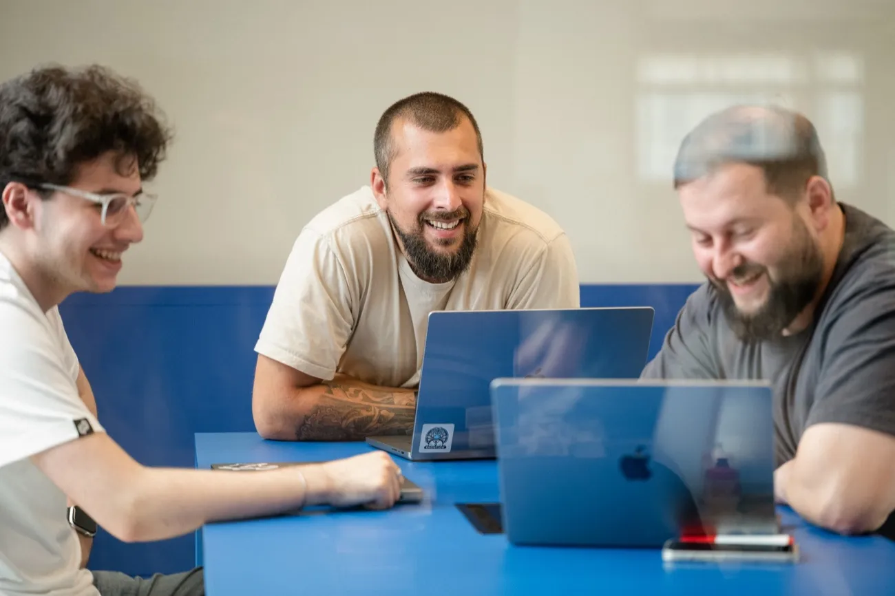 Three colleagues laughing together at a table with laptops