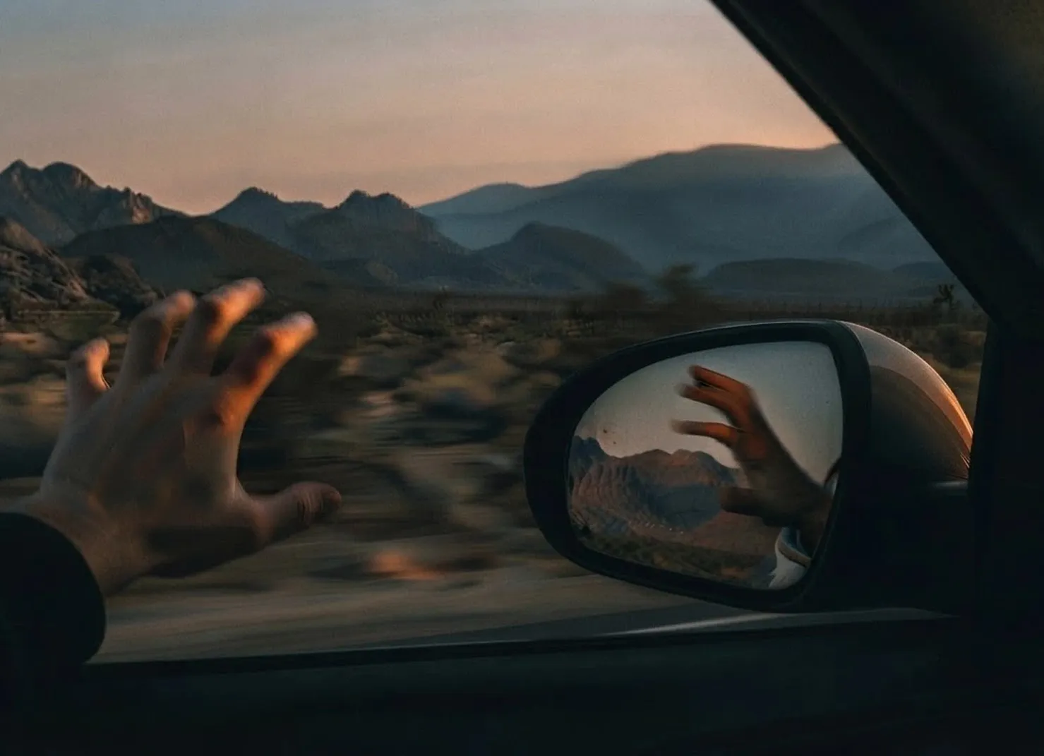Hand aus dem Autofenster bei Sonnenuntergang