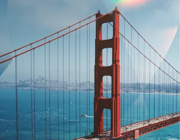 The Golden Gate Bridge spans turquoise waters with a cityscape in the background, under a clear blue sky.
