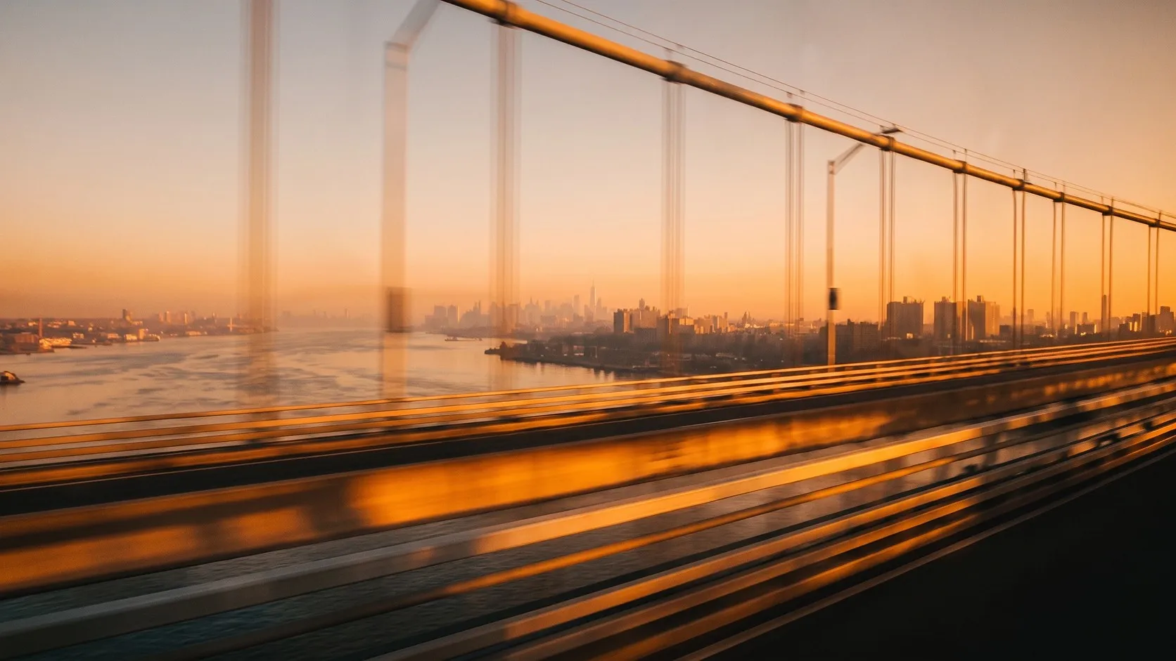 View from a suspension bridge at sunset, with a city skyline in the distance