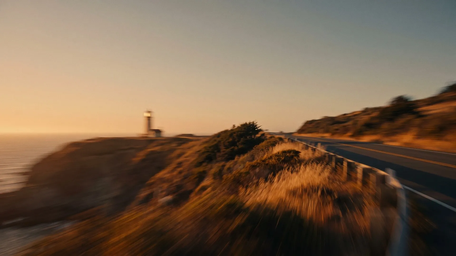 Coastal road leading past a lighthouse on a cliff at sunset