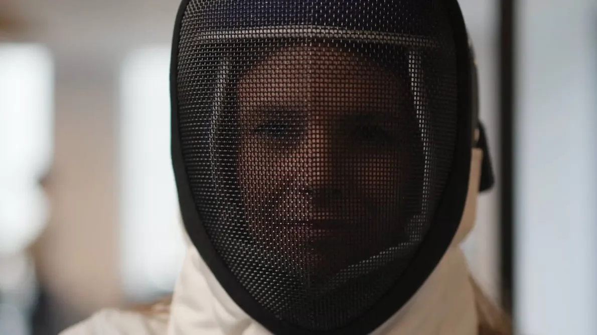 A person wearing a fencing mask, with the mesh covering their face.