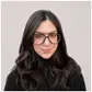Person with long dark hair and large glasses, wearing a black turtleneck, smiles softly against a light background.