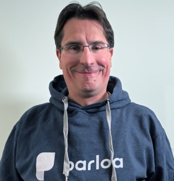 Smiling person wearing glasses and a blue hoodie with the logo "parloa" on it, set against a plain background.