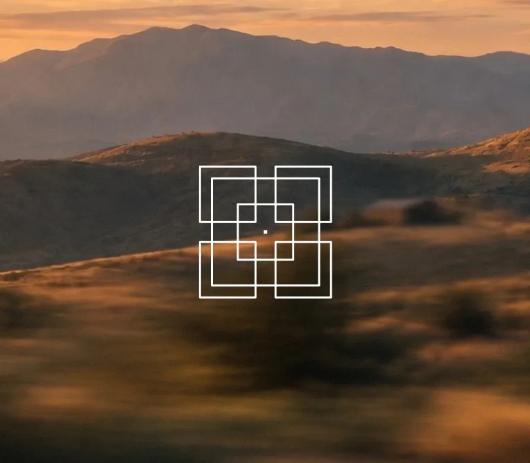 Ineinandergreifende weiße Quadrate als Symbol für Composability vor einer Berglandschaft bei Sonnenuntergang