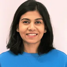 Smiling person with shoulder-length black hair wearing a blue top against a light background.