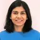 Smiling person with shoulder-length black hair wearing a blue top against a light background.