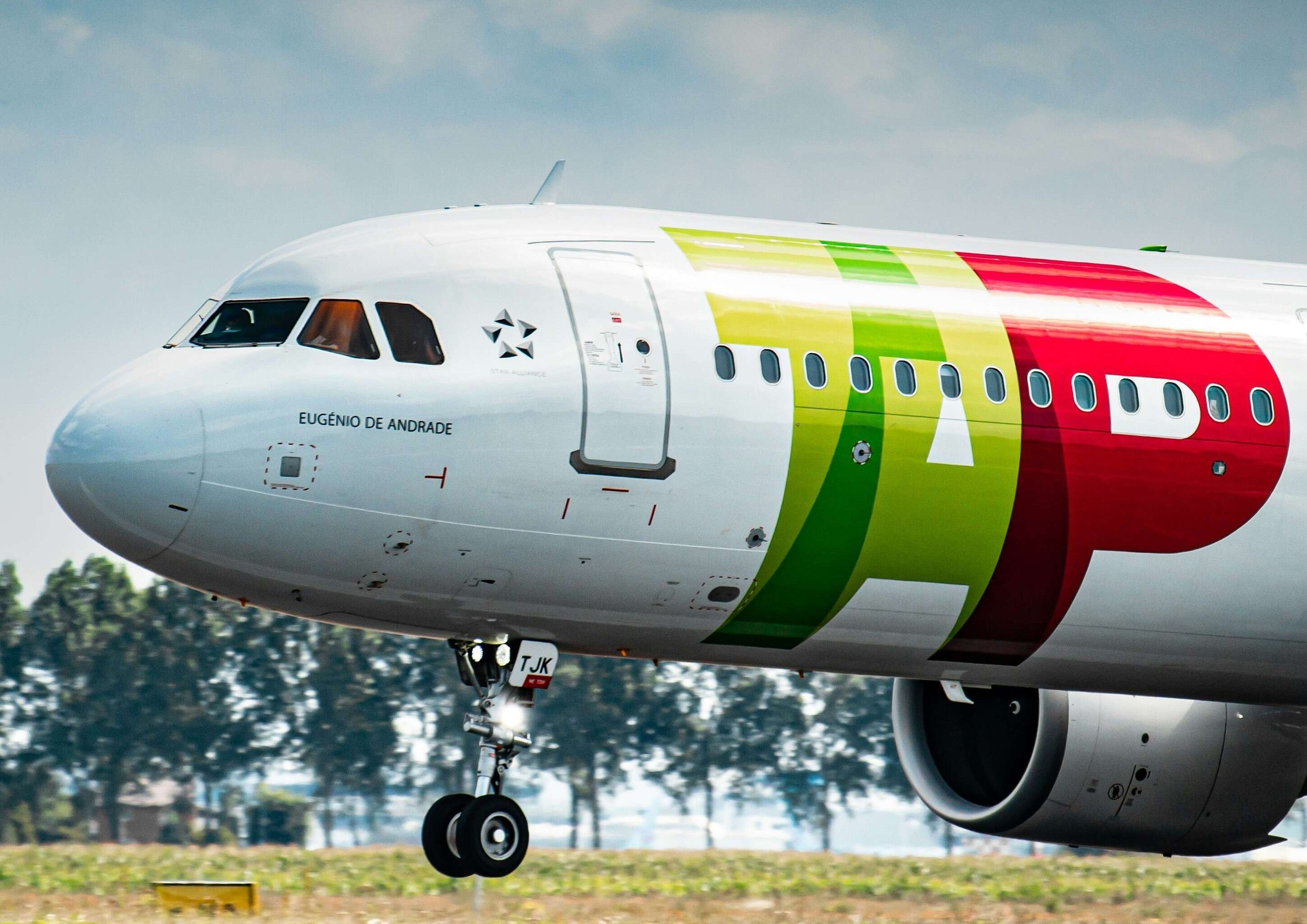 Close-up of an airplane nose with "Eugénio de Andrade" written on it, showing landing gear and colorful TAP Air Portugal livery.