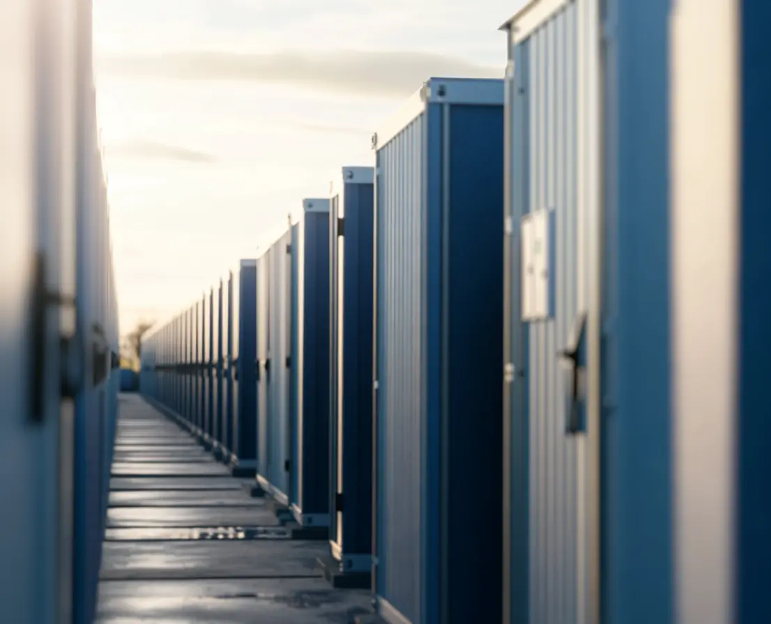 A row of industrial storage units in blue, aligned along a pathway, with a bright sky in the background.